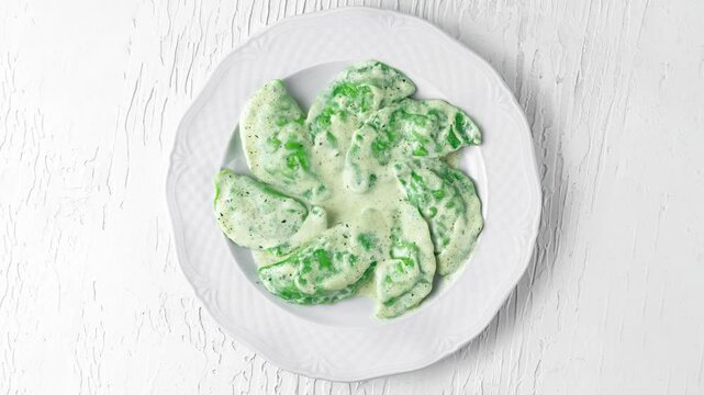 plate with green spinach and bryndza dumplings rotating top view on white wooden background