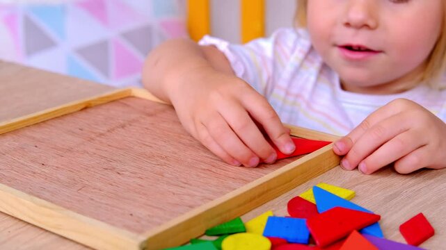 Litle cute child, girl plays with colored wooden geometric figures, cubes, builds houses and animals, counts details, concept of development of creativity, fine motor skills, patience perseverance