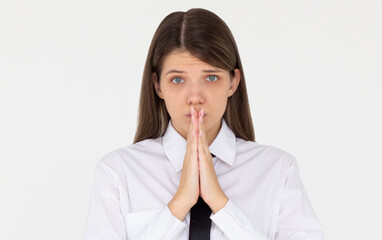 Portrait of imploring girl tilts head, purses lips, looks sadly at camera, makes praying gesture,...
