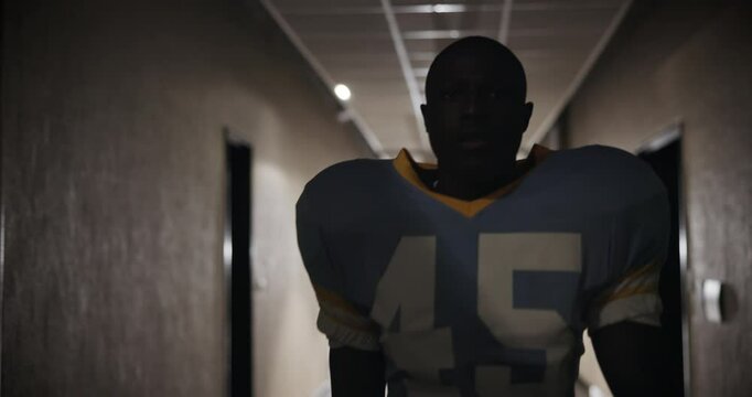 Football player, man and walking through tunnel in stadium for tournament, match and ready for competition. American contact sport, face and professional athlete in cloakroom corridor after half time