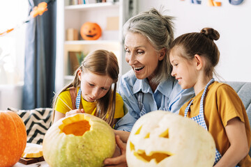 Happy grandmother and granddaughters carving pumpkins together for halloween celebration