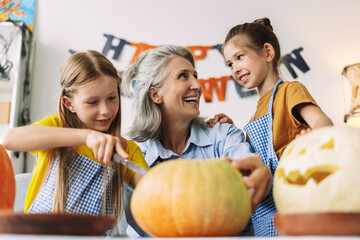 Little girls and mature woman holding knif, carving pumpkins together for halloween celebration