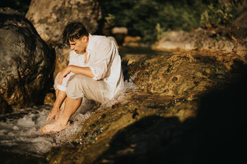 A young man sits in a serene mountain stream, enjoying the natural beauty and tranquility of the environment.