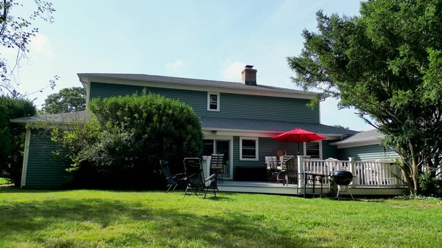 Drone staying close to the ground moving closer to a backyard deck with furniture set up for a party.