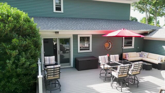 Panning away from a set up backyard deck with a red umbrella and cushions on the furniture.