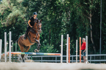 A young equestrian jumps over a hurdle with her horse during a training session in an outdoor...