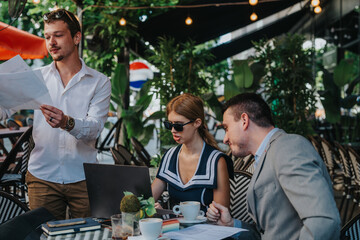 Business professionals conducting an outdoor meeting, discussing documents and collaborating on a laptop at a cafe, creating a relaxed yet productive atmosphere.