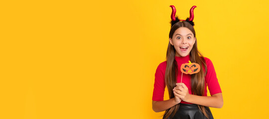 surprised teen girl wearing imp horns holding pumpkin party accessory on yellow background, party....