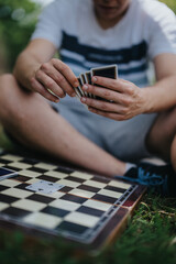 Close-up of a person playing cards outside, sitting cross-legged with a checkerboard. The image captures a relaxing outdoor leisure activity on a sunny day.