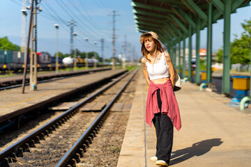 Young Asian woman enjoy outdoor lifestyle road trip travel by railway transportation on summer holiday vacation. Attractive girl standing by railroad track during waiting for train at railway station.