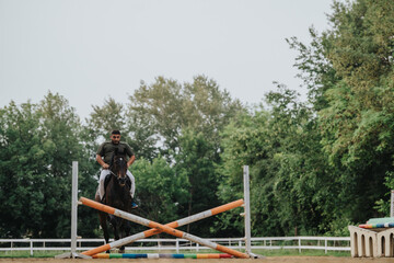 Male rider and horse competing in an equestrian jumping event in an outdoor arena surrounded by...