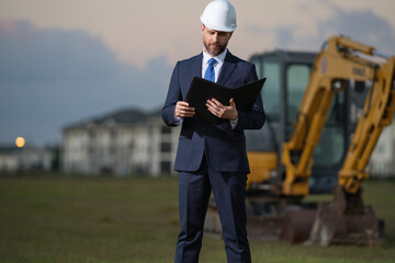 Civil engineer worker at a construction site. Engineer man in front of house background. Confident engineer worker at modern home building construction. Hispanic civil engineer in helmet.