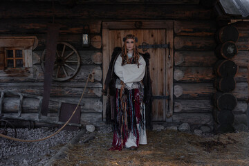 Shamanic dances, a shaman woman in a folk costume with lots of fringes and ribbons, in a village among wooden architecture, Slavic or Nordic style