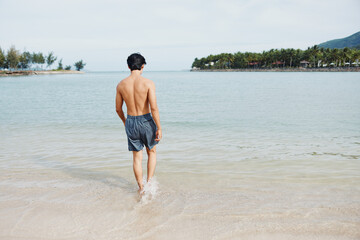 Swim Fun Under the Tropical Sun: Happy Asian Man Enjoying Water Sports and Relaxation on a Blue Beach Vacation