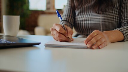 Teleworker at desk transcribing data from laptop to notepad, finalizing project. Remote worker solving job tasks before deadline, writing info on paper using pen, camera A close up panning shot