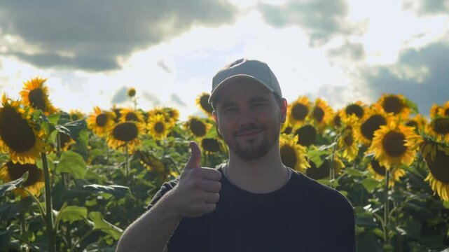 Young Mexican farmer is smiling and giving a thumbs up against backdrop of a field of sunflowers and cloudy sky, foreshadowing imminent rain that would be beneficial for harvest.