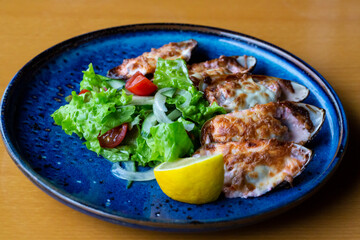 Seafood. Shellfish mussels. Baked mussels with cheese, cilantro and lemon in shells on cast iron black plate. Plate of mussels, cold white wine, lemon and cilantro on old wooden blue background.