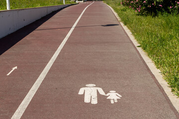 Pedestrian lane sign showing adult and child holding hands painted on paved path