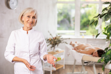 In spa office there is elderly woman nurse dressed in medical uniform, suit. Advertising poster, banner for salon of cosmetology and massage services