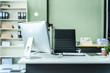A sleek modern desk with a computer and laptop sits empty in a glass office, reflects a contemporary style with no people present, emphasizing a clean, professional environment.