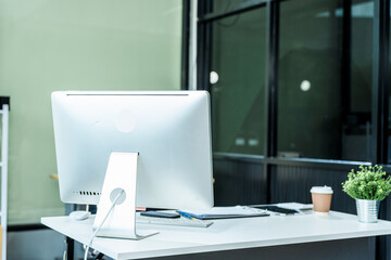A sleek modern desk with a computer and laptop sits empty in a glass office, reflects a contemporary style with no people present, emphasizing a clean, professional environment.
