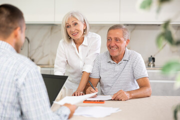 Couple of elderly man and woman while discussing deal with male salesman in kitchen