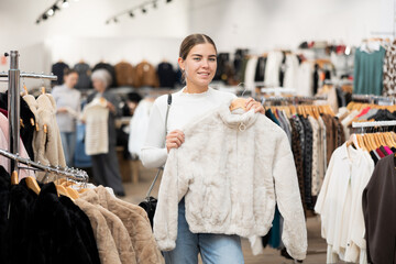 Fototapeta premium Young cheerful girl demonstrates fur coat in a clothing boutique