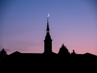 Crescent moon over silhouetted church steeple cross dusk dawn europe