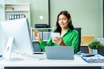 successful and happy young Asian businesswoman in a formal suit works at her desk in a modern glass office. consults on business strategies LGBTQ inclusivity, managing multiple projects efficiently.