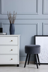 Stylish interior with stool and chest of drawers near light grey wall