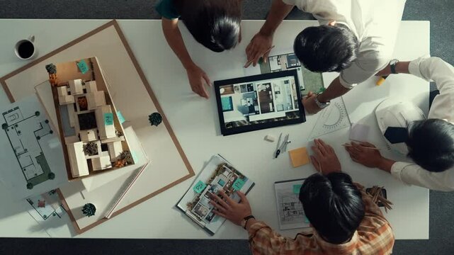 Time lapse of designer looking at model while discussing about building. Top view of architect engineer explaining idea while talking and writing blue print scattering at meeting table. Alimentation.