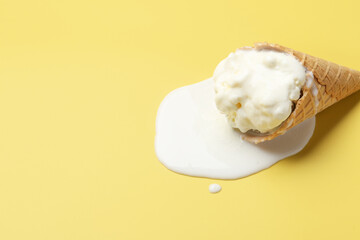 Melted ice cream in wafer cone on yellow background. Space for text