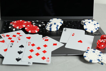 Online poker. Playing cards, chips, dice and laptop on light grey table