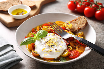 Delicious fresh burrata salad in bowl served on gray textured table, closeup