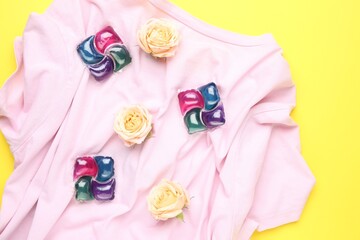 Laundry detergent pods, t-shirt and flowers on yellow background, flat lay