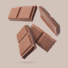 Pieces of sweet chocolate falling on beige background