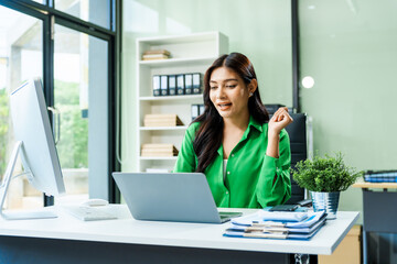 Fototapeta premium successful and happy young Asian businesswoman in a formal suit works at her desk in a modern glass office. consults on business strategies LGBTQ inclusivity, managing multiple projects efficiently.