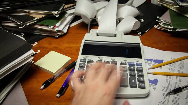 Time lapse of a man's hand using a calculator on a cluttered office desk.