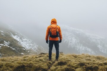 Obraz premium Person in Orange Jacket Looking at Snow-Capped Mountains in Scenic Foggy Morning