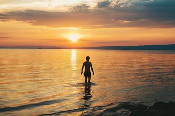 Silhouette of person walking in calm ocean water during a golden sunset with serene sky