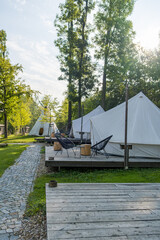 Camping tents set up in a forest with wooden platforms and outdoor furniture