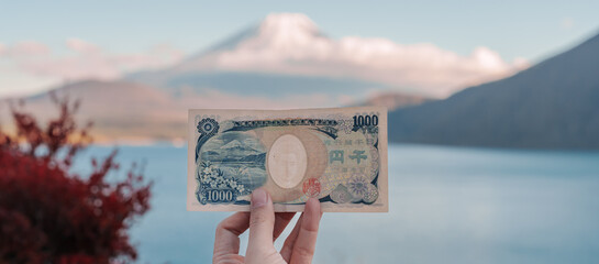 Hand holding 1000 yen banknote with mount Fuji at Lake Motosu, happy tourist travel Mt Fuji and...
