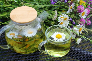 On the table there is a glass teapot and a cup of chamomile infusion.	