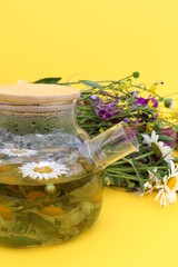 There is a teapot with chamomile infusion on a yellow background.