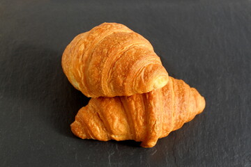 Two croissants lie on a black stone background.