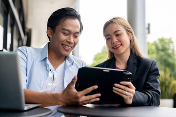A smart Asian businessman is discussing a project with his assistant at an outdoor table.