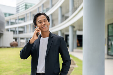 A successful Asian businessman is standing in an outdoor hallway and talking on the phone.