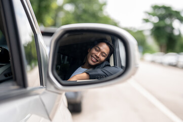 A close-up image of a car's wing mirror with a man in a business suit smiling in the reflection.