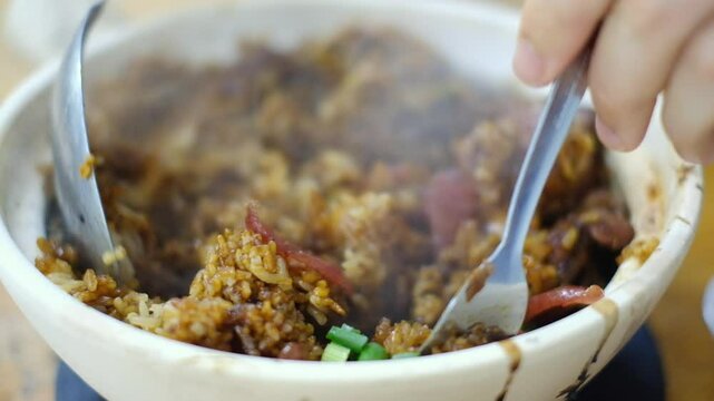 Man mixing bowl of Heung Kee claypot chicken rice with glutinous rice, lap cheong (Chinese sausage), salted fish, spring onion cooked on a traditional charcoal stove - Pudu, Kuala Lumpur, Malaysia