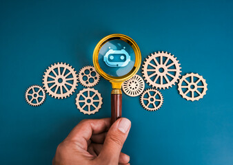 AI searching tools, development and management technology assistance service support concept. Bot icon in magnifying glass lens in human hand surrounding many gear and cogwheel, on blue background.